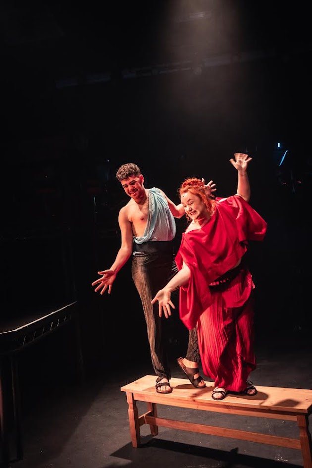 Jess in a red robe performing a dramatic stage scene under theatre lighting