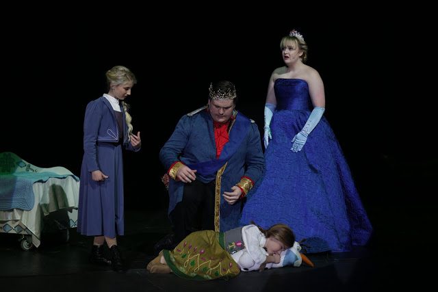 Stage scene with three costumed performers in a darkened set